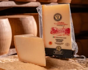 Punta di Parmigiano Reggiano 12 mesi fresca posizionata sopra una forma intera.