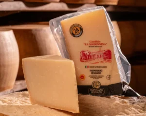 Spicchio di Parmigiano Reggiano 24 mesi friabile su una forma di formaggio.
