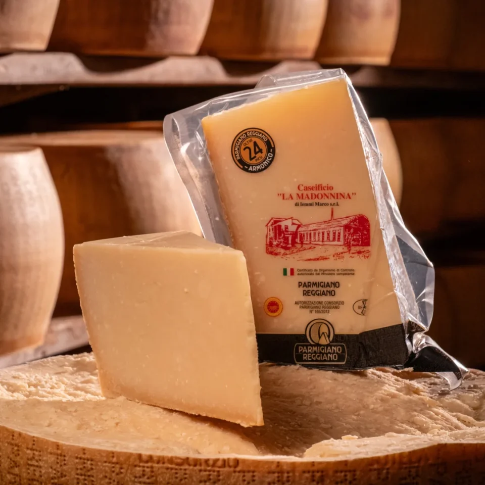 Spicchio di Parmigiano Reggiano 24 mesi friabile su una forma di formaggio.