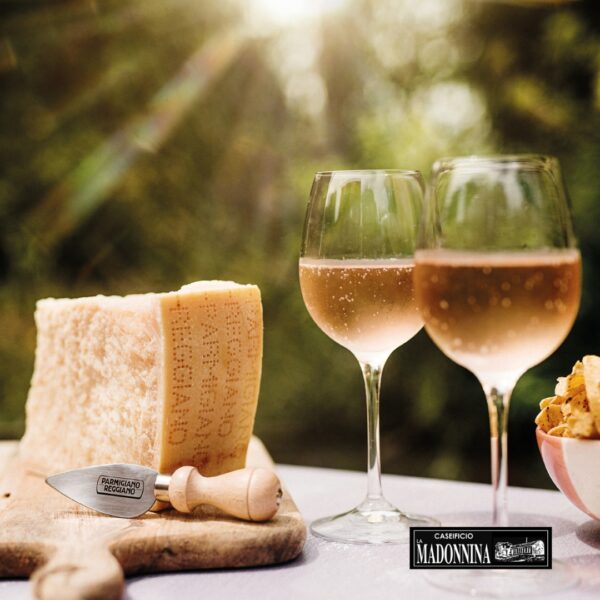 CASEIFICIO LA MADONNINA - Aperitivo perfetto con Parmigiano Reggiano - Two glasses of rose wine next to a block of Parmigiano Reggiano cheese and a cheese knife.