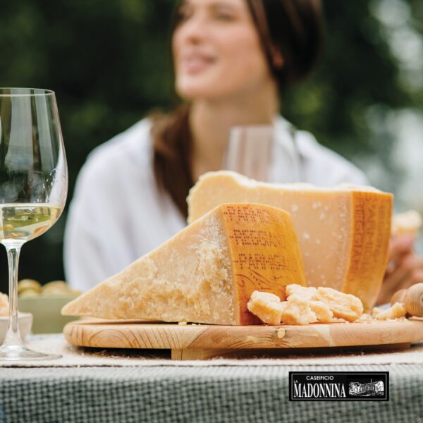 CASEIFICIO LA MADONNINA - Aperitivo perfetto con Parmigiano Reggiano - Two types of cheese on a wooden board with a glass of white wine nearby, outdoors.