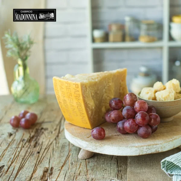 CASEIFICIO LA MADONNINA - Frutta fresca e Parmigiano Reggiano - A wedge of cheese on a wooden board, with red grapes and small cheese cubes beside it.